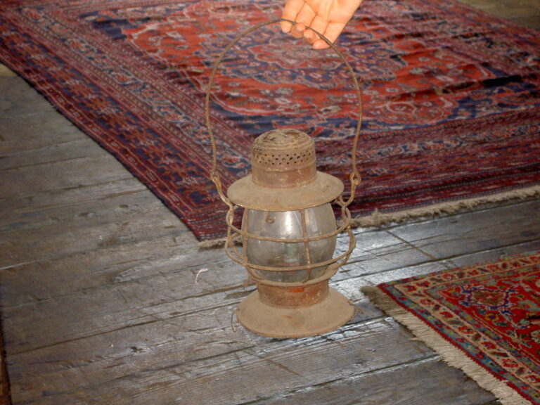 rusted lantern with glass windscreen held over a wooden floor with traditional rugs