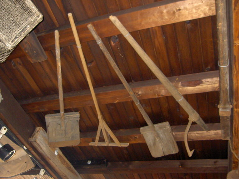 two wooden shovels, a wooden rake and a peavey suspended from beams